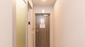 A narrow hallway with a wooden floor, a door with a sign above it, and a light fixture on the ceiling. - Tora Hotel Nishikamata (Ota City)