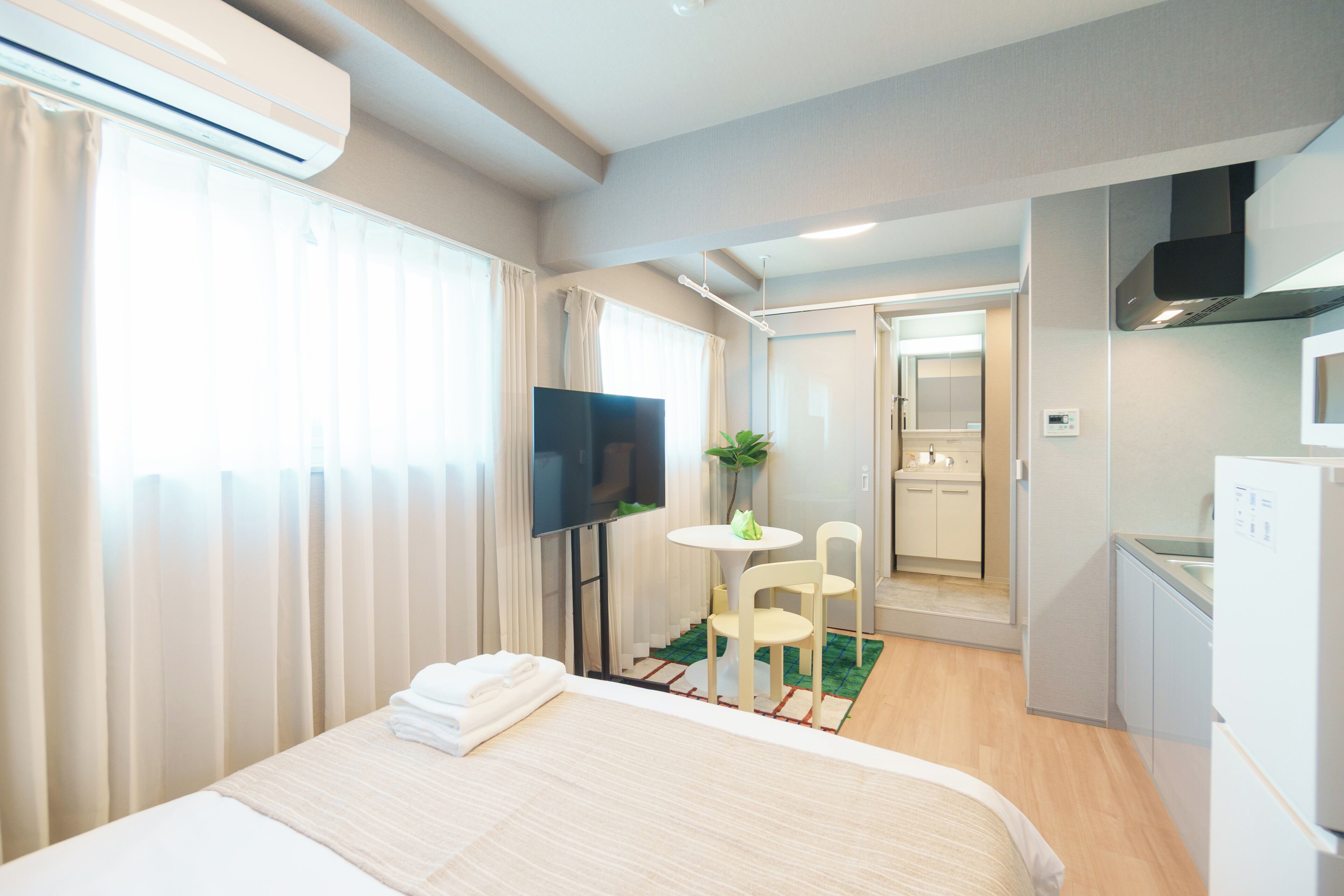 Una habitación de hotel con cama, televisor, una pequeña mesa con sillas, una planta y un rincón americano.