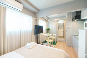 A hotel room with a bed, a TV, a small table with chairs, a plant, and a kitchenette. - Tora Hotel Nishikamata (Ota City)