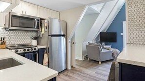 Una cocina equipada con microondas, estufa, refrigerador y una zona de comedor con sofá y televisor.