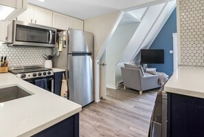 A kitchen with a microwave, stove, refrigerator, and a dining area with a sofa and TV.