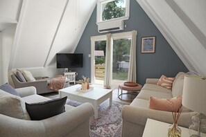 A modern living room with a sloped ceiling, a flat-screen TV mounted on the wall, a white coffee table, and a beige sofa.