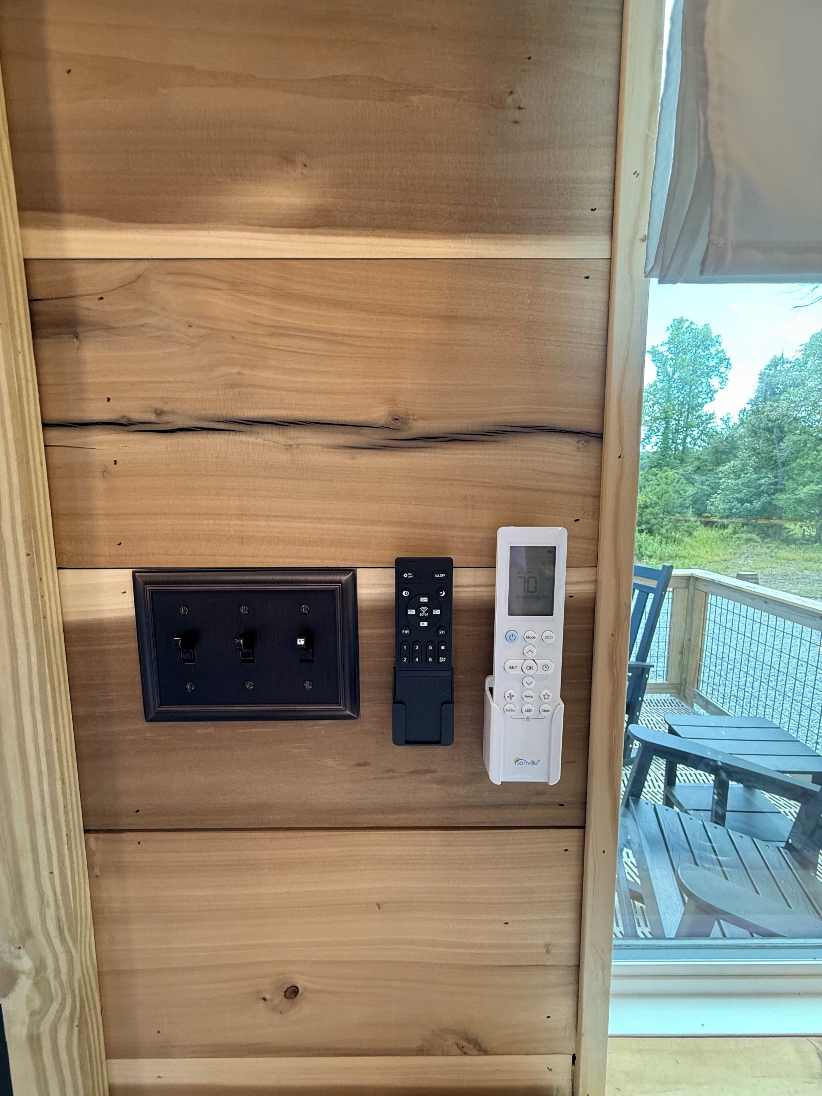 A wooden wall with a power outlet, a remote control, and a digital thermostat.