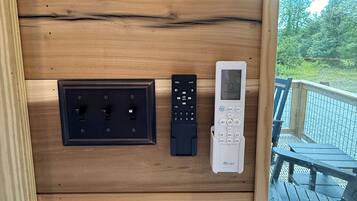 A wooden wall with a power outlet, a remote control, and a digital thermostat.