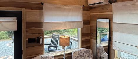 A cozy interior with wooden paneling, a round table with a lamp, two upholstered chairs, and a large window with a view.