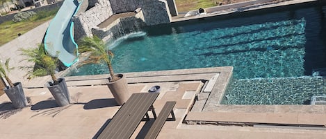 A swimming pool with a slide, surrounded by a stone wall and a picnic table.