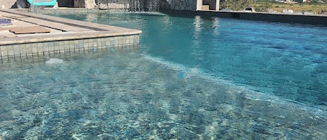 A clear pool with a stone wall and a blue chair.