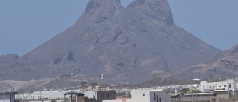 Un paisaje montañoso con un pico destacado y un pequeño asentamiento con edificios modernos en primer plano.