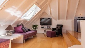 Um apartamento loft moderno e compacto, com teto inclinado, TV de tela plana na parede, pequena área de jantar e cozinha compacta.