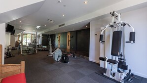 Uma academia com diversos equipamentos de ginástica, uma televisão e um banco.