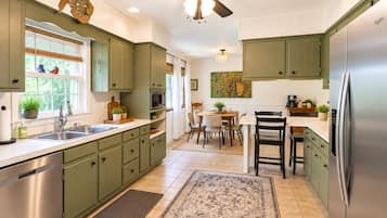 Una cucina con mobili verdi, un frigorifero in acciaio inossidabile, una ventola a soffitto e un'area pranzo con tavolo e sedie.