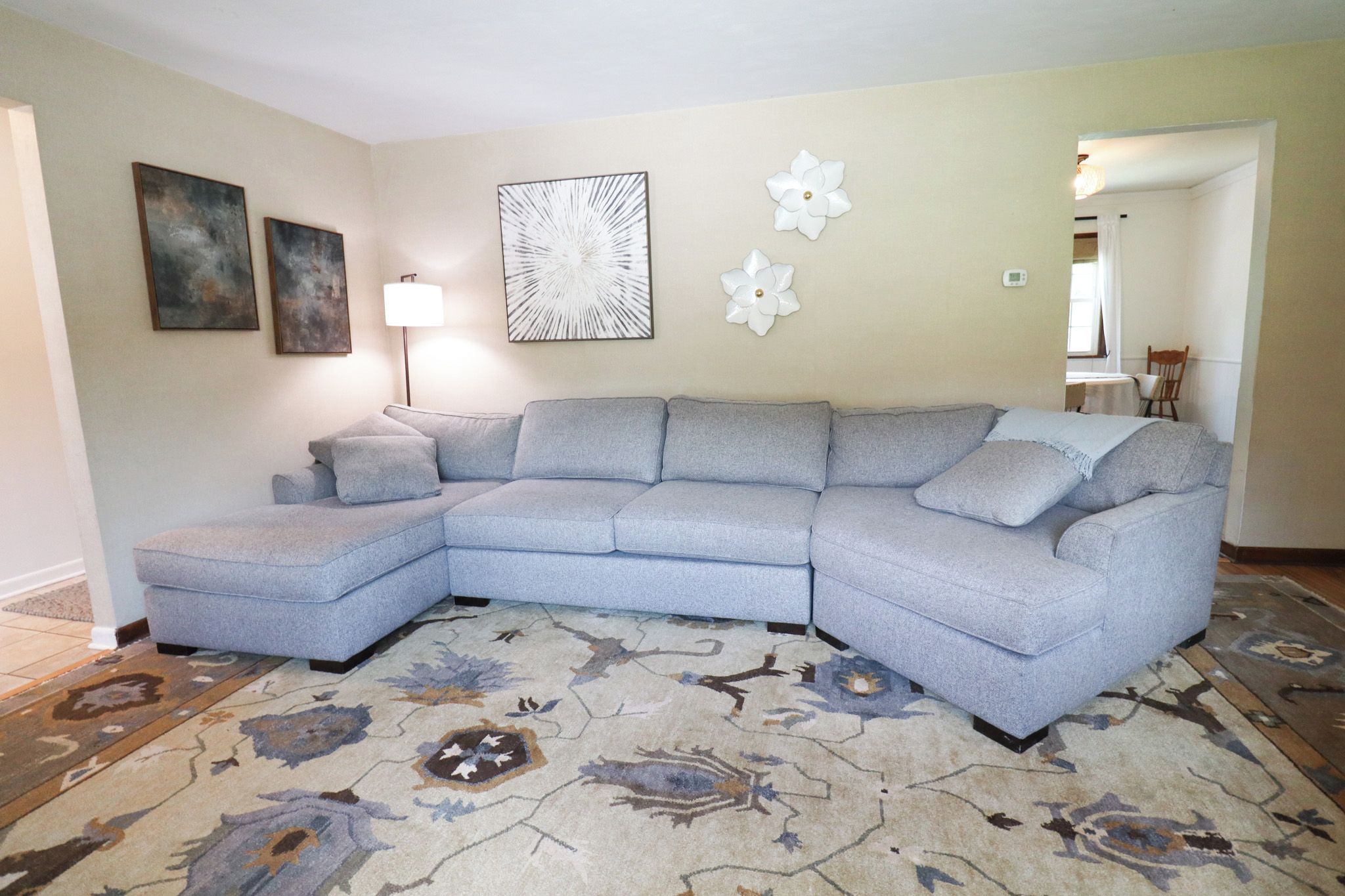 A living room with a sectional sofa, a patterned rug, wall art, and a lamp.