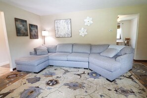 Ein Wohnzimmer mit Ecksofa, einem gemusterten Teppich, Wandbildern und einer Lampe.