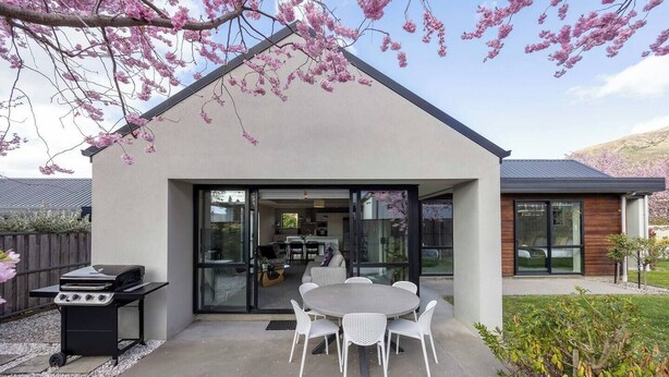 A modern house with a patio, a barbecue grill, and a dining area with white chairs. - Mountain views in Meadowstone (Wānaka)