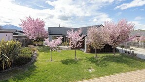 A residential area with modern houses, a well-maintained lawn, and cherry blossom trees. - Mountain views in Meadowstone (Wānaka)