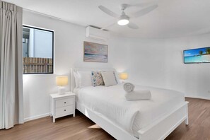 A bedroom with a bed, nightstands, a ceiling fan, and artwork on the walls. - 1 Jade Court - Centrally Located, Brand New Furnishings (Maroochydore)