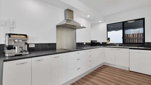 A modern kitchen with white cabinetry, a built-in espresso machine, a large window, and a wooden floor. - 1 Jade Court - Centrally Located, Brand New Furnishings (Maroochydore)
