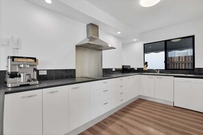 Eine moderne Küche mit weißen Schränken, einer integrierten Espressomaschine, einem großen Fenster und Holzboden.