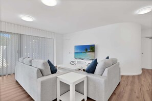 Uma sala de estar moderna com um conjunto de sofás, uma mesa de centro e uma televisão de tela plana em uma parede branca.