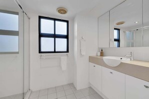 Ein modernes Badezimmer mit großem Fenster, einem weißen Waschbecken und einem Spiegel.