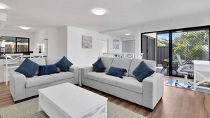 A modern living room with two grey sofas, a white coffee table, and a dining area with a white table and chairs. - 1 Jade Court - Centrally Located, Brand New Furnishings (Maroochydore)