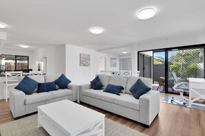 Ein modernes Wohnzimmer mit zwei grauen Sofas, einem weißen Couchtisch und einem Essbereich mit Tisch und Stühlen in Weiß.