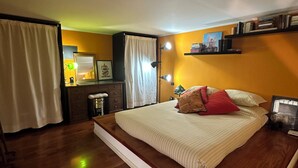 Une chambre à coucher avec un grand lit, un plancher en bois, une table de chevet, une lampe et une étagère remplie de livres.