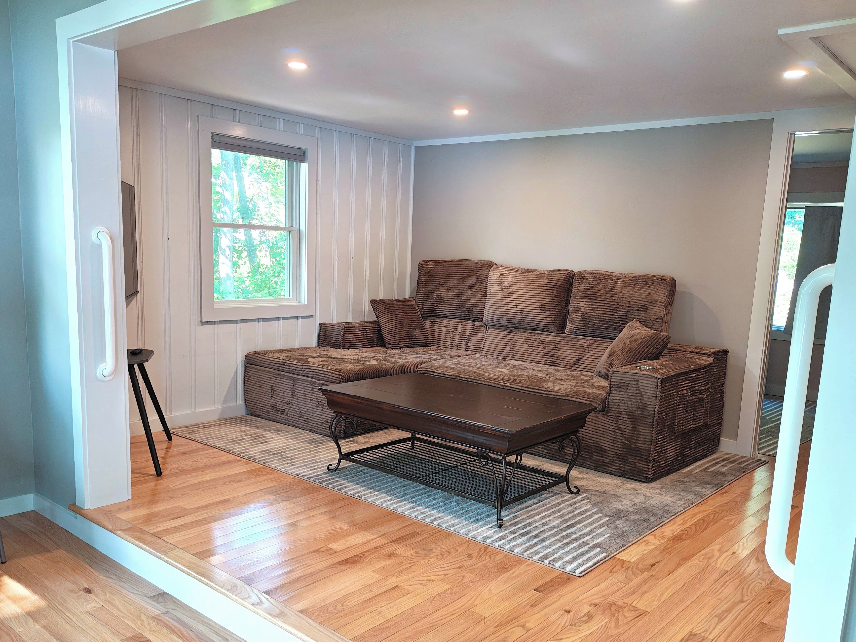 A room with a brown sofa, a wooden coffee table, and a window with blinds.