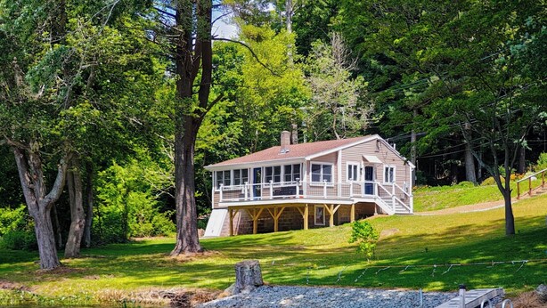 A lakeside house with a deck, surrounded by trees and a dock.