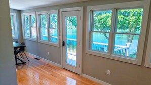 A room with large windows, a wooden floor, and a view of a deck and water.