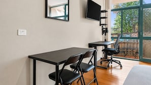 Ein modernes Zimmer mit Schreibtisch, zwei Stühlen, Fernseher und großen Fenstern.