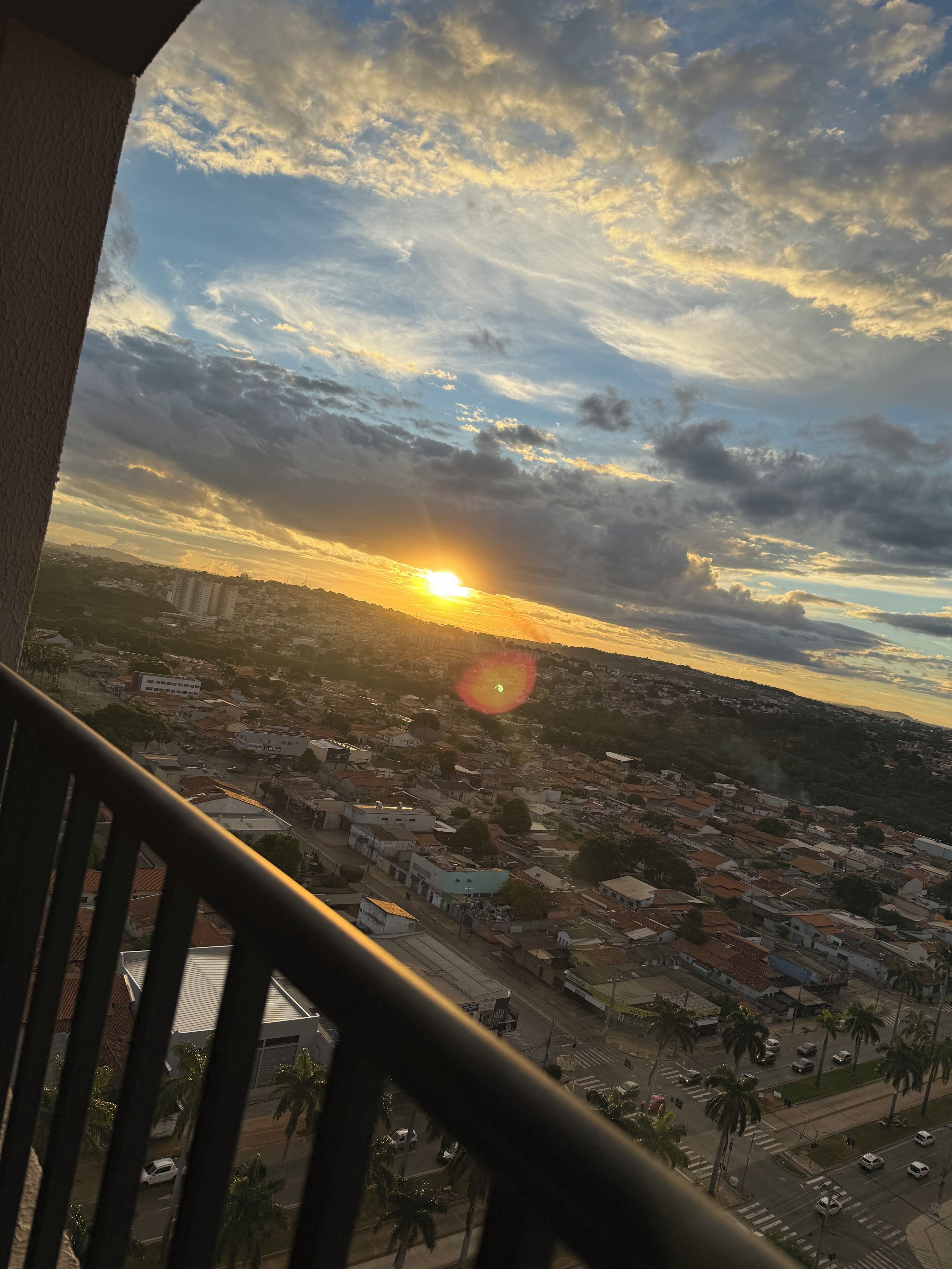 Un paisaje urbano con un atardecer, edificios y una calle bordeada de palmeras.