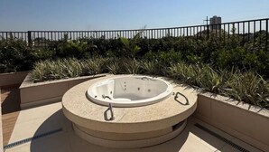 A circular hot tub on a rooftop terrace with a metal railing and greenery in the background. - 2-bedroom apartment, close to the 44th Street area, bus station, airport, and Flamboyant Shopping Mall. (Goiânia)