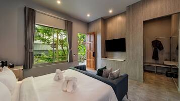 Quarto de hotel moderno com uma cama grande, um sofá, uma TV e vista para o verde lá fora.