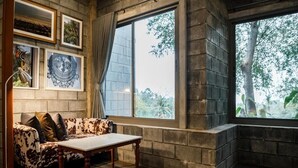 A room with a stone wall, a large window with a view of trees, a sofa with patterned cushions, and a table. - PhlaidamhillSichon (Sichon)