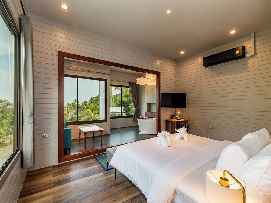 Ein modernes Hotelzimmer mit einem großen Bett, einem Schreibtisch, einem Stuhl, einem Fernseher und einem Balkon mit Blick auf Grünflächen.
