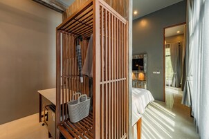 A room with a wooden wardrobe, a bed, a small table, and a mirror.