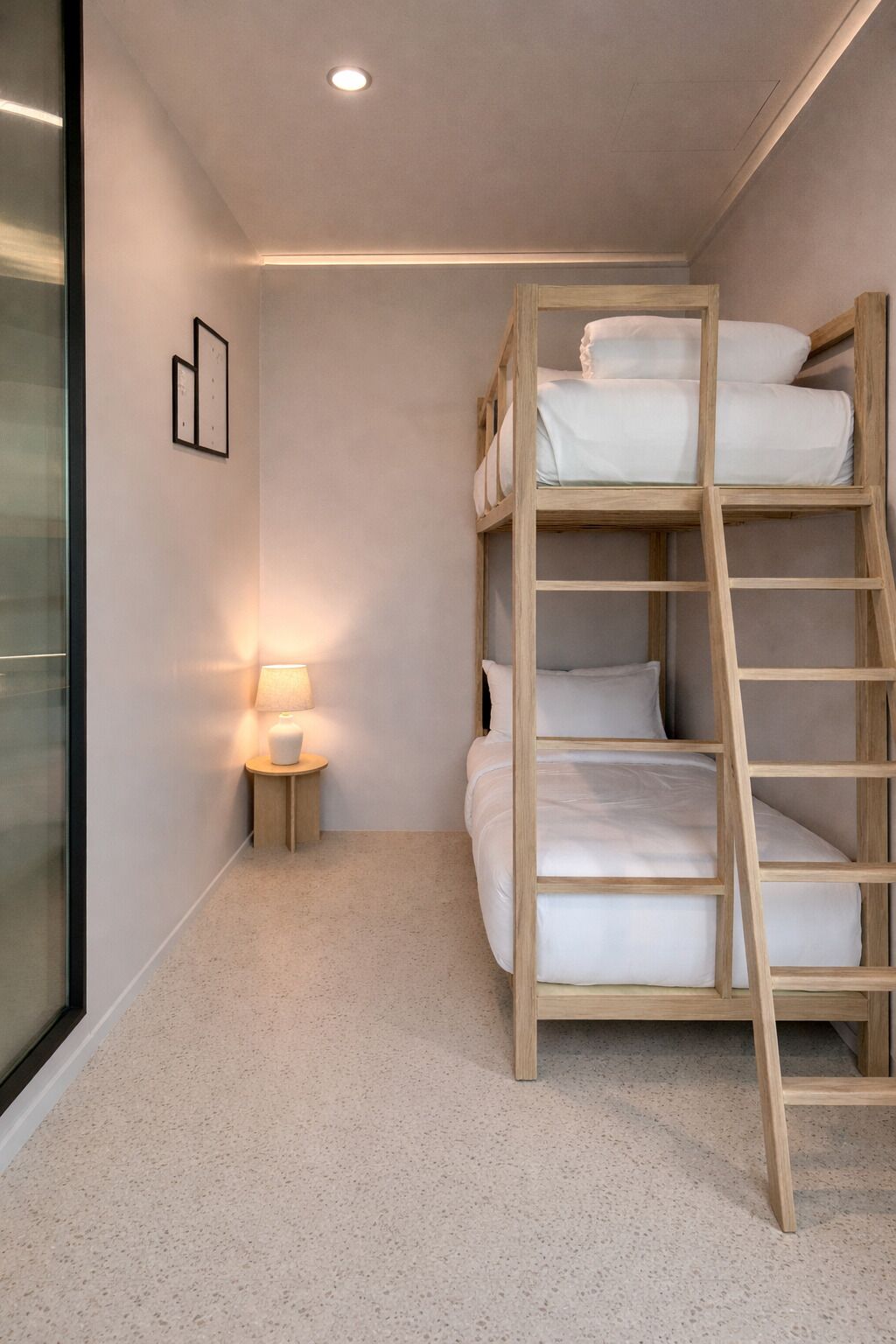 Una cama individual en literas en una habitación con una mesita de noche pequeña, una lámpara y un cuadro en la pared.