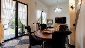 Un espace repas comprenant une table ronde, des chaises, un lustre, un téléviseur et une porte-fenêtre coulissante donnant sur un espace extérieur.