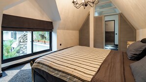 Une chambre à coucher avec un grand lit, un lustre, une fenêtre donnant sur un beau paysage et un escalier menant à une autre pièce.