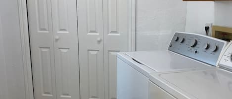 A laundry room with a front-loading washer and dryer, wooden flooring, and white double doors.