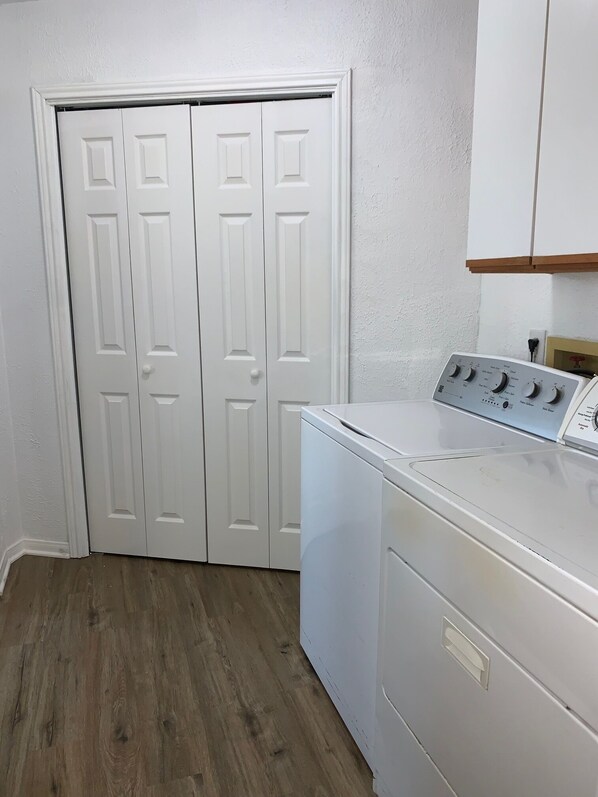 A laundry room with a front-loading washer and dryer, wooden flooring, and white double doors.