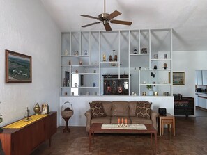 A living room with a sofa, a coffee table, a bookshelf, a ceiling fan, and a painting on the wall. - The Country Nook-Rustic Charm & Starry Nights! (Temple)