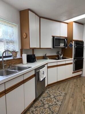 A modern kitchen with white cabinets, stainless steel appliances, a microwave, and a built-in oven. - The Country Nook-Rustic Charm & Starry Nights! (Temple)