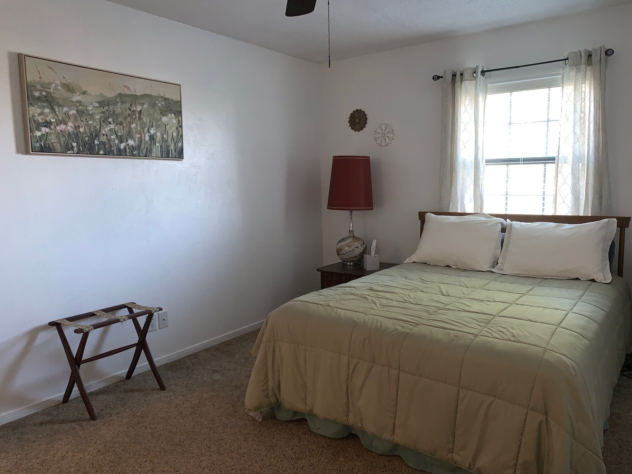 Una camera da letto con un letto, un comodino, una lampada, un quadro e una finestra con tende.