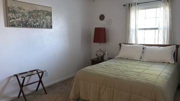 Una camera da letto con un letto, un comodino, una lampada, un quadro e una finestra con tende.