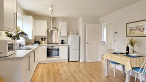 Cocina compacta con gabinetes blancos, extractor de acero inoxidable, microondas, horno y refrigerador.