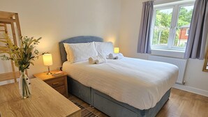 Un dormitorio con cama, mesitas de noche, lámpara, un florero con flores, una ventana con cortinas y vistas al exterior.
