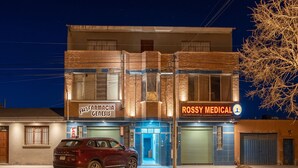A building with a pharmacy and a medical clinic on the ground floor, a parked car, and a tree.