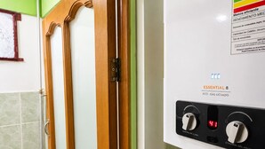 A bathroom with a white water heater, control knobs, and a door with a wooden frame.